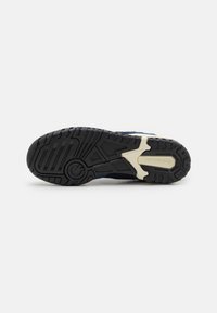 Semelle de basket avec un motif noir et beige, conception non marquante, et le logo "new balance" sur la section beige du milieu du pied.