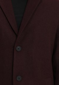 Blazer bordeaux in tessuto texturizzato con revers a punta, due bottoni neri e una tasca frontale. Adatto per abbigliamento formale.