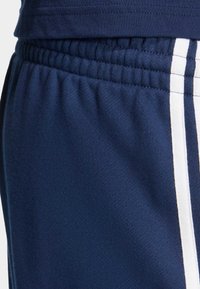 Tmavomodré športové nohavice s jemnou textúrou, na boku s bielymi vertikálnymi pruhmi. Elastický pás pre pohodlné nosenie.