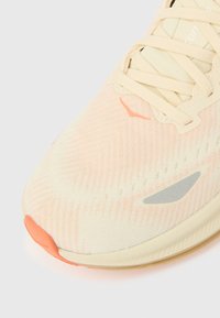 Αθλητικό παπούτσι με ελαφρώς κίτρινη κα ι ροδακινί επάνω επιφάνεια με διαμάντι μοτίβο, γκρι σημεία και πορτοκαλί προστατευτική μύτη. Ίσια κορδόνια και μαλακή σόλα.