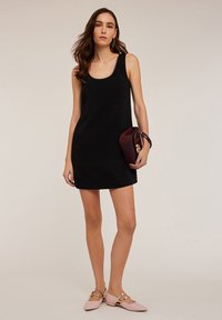 Schwarzes ärmelloses Kleid mit einem runden Ausschnitt, das eine figurbetonte Silhouette hat. Begleitet von einer weinroten Clutch und flachen Schuhen in Blush-Farbe.