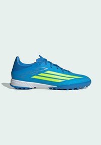 Chaussure de football bleue avec des rayures jaune néon, semelle texturée pour gazon, design à lacets et détail de semelle intermédiaire blanche.
