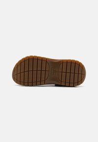 Semelle de chaussure en caoutchouc marron avec motif quadrillé et logo Crocs embossé au centre.