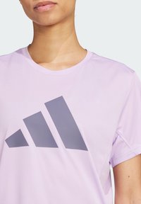 Valkoinen urheilupaita, jossa on suuri tummanharmaa Adidas-logo rinnassa. Paita on valmistettu sileästä materiaalista ja siinä on pyöreä kaula-aukko.