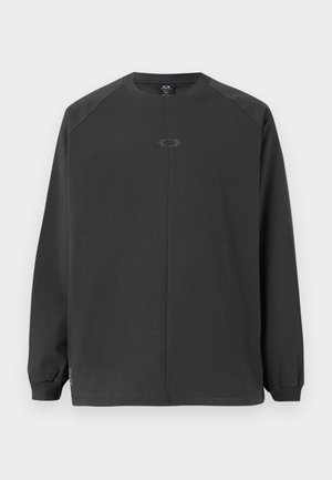 Mørkegrå langermet skjorte laget av mykt materiale, med raglanermer og en enkel logo i midten. Mansjettene er elastiske.