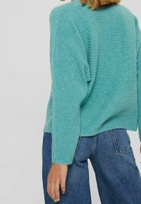 Pull turquoise côtelé à coupe décontractée, avec épaules tombantes et manches longues, porté avec un jean denim bleu.