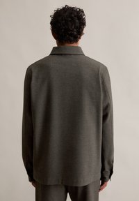 Ciemnozielona, teksturowana koszula z kołnierzykiem i długimi rękawami, o luźnym kroju i z zapięciem na guziki przy mankietach, pokazana z tyłu.