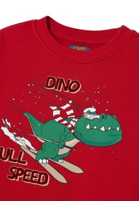 Roter Pullover mit einem grünen Dinosaurier, der Ski fährt. Das Design umfasst einen weiß-rot gestreiften Schal, den Text "DINO VOLL GAS" und Schneeflocken.