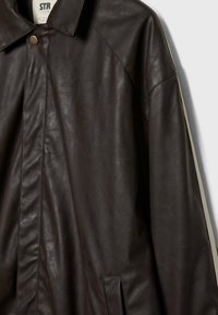 Veste en similicuir marron foncé avec col, boutons avant dissimulés et poche latérale verticale sur fond uni.