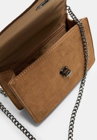 Sac bandoulière en simili cuir marron avec texture matelassée, quincaillerie en ton argent, chaîne en bandoulière et poche intérieure zippée.
