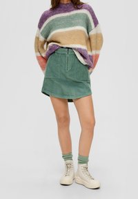 Jersey de rayas multicolores en suave punto, combinado con una mini falda de pana verde con cremallera delantera y bolsillos. Zapatillas altas blancas.