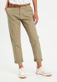 Khaki chinos z podwiniętymi nogawkami, wykonane z lekkiego materiału. Połączone z plecionym brązowym paskiem i białymi sneakersami z beżowymi akcentami.