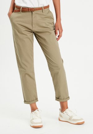 Chino kaki avec les poignets retroussés, fabriqué en tissu léger. Associé à une ceinture en cuir tressée marron et des baskets blanches avec des accents beige.
