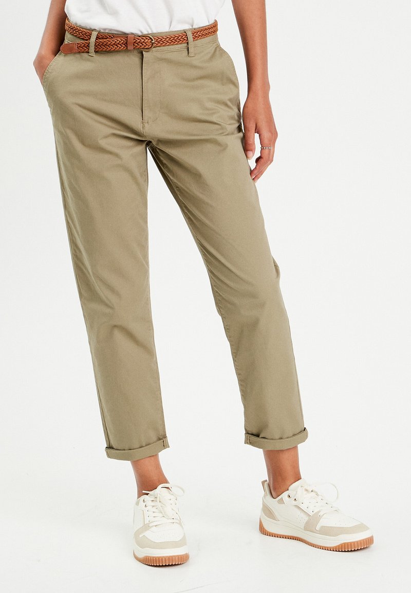 Khaki chinos z podwiniętymi nogawkami, wykonane z lekkiego materiału. Połączone z plecionym brązowym paskiem i białymi sneakersami z beżowymi akcentami.