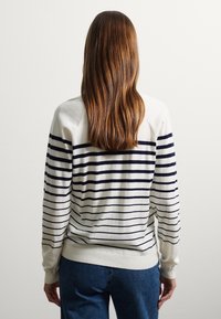 Maglione a manica lunga di colore crema con strisce orizzontali blu navy. Presenta un collo a giro e maniche lunghe. Tessuto a maglia morbido con orlo e polsini a coste.