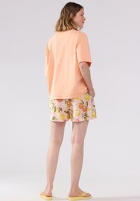 T-shirt di cotone color pesca chiaro, abbinata a pantaloni corti rosa con motivi di agrumi. Design semplice, vestibilità casual, indossata con sandali gialli.