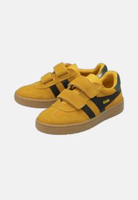 Zapatos de ante amarillos con rayas negras, con dos tiras de velcro, puntera redonda y suela de goma texturizada. Logo de Gola visible.