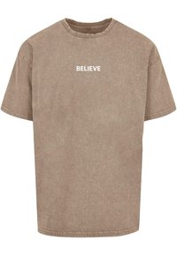 Brūns kokvilnas T-krekls ar apaļu kakla izgriezumu, īsām piedurknēm un nolietotu tekstūru. Priekšpusē ir balta uzraksts "BELIEVE".