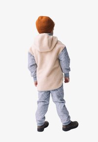 Beige Fleece-Hoodie mit grauen gesteppte Ärmeln, dazu passende graue gesteppte Hosen und braune Stiefel. Das Kind steht mit dem Rücken zum Betrachter.
