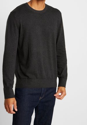 Dunkelgrauer Rundhals-Pullover aus weichem Stoff, mit gerippten Bündchen und Saum. Getragen über dunkelblauen Jeans.