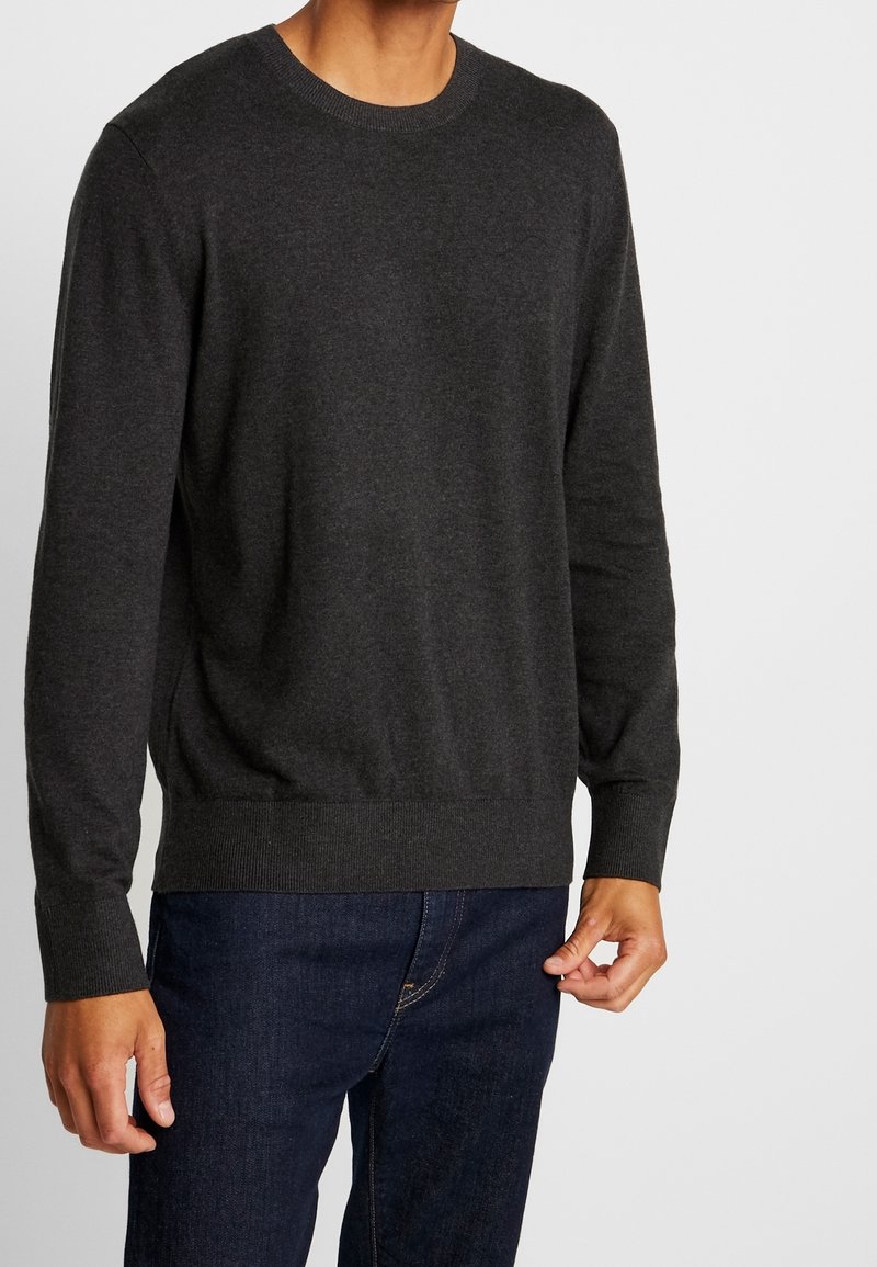 Maglione a girocollo grigio scuro in tessuto morbido, con polsini e bordo a costine. Indossato sopra jeans in denim scuro.