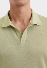 Polo vert clair avec un tissu texturé. Présente un col en V et un détail de col intérieur contrastant. Surface lisse avec une coupe décontractée.