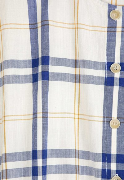 Tissu blanc avec un grand motif à carreaux en lignes bleues et marron clair, et des boutons beiges le long d'une couture verticale.
