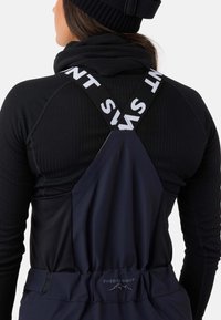 Marineblåt udendørs overall med justerbare krydsede stropper, der har hvid tekst. Glat stof, elastisk talje og logodetalje på ryggen.