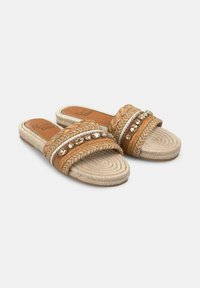 Sandali marroni a slip-on con cinturini intrecciati e accenti metallici decorativi, dotati di una suola intrecciata testurizzata e una soletta piatta.
