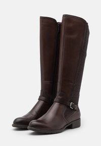 Brązowe skórzane kozaki za kolano z bocznym zamkiem błyskawicznym, teksturowanym panelem z siateczki i paskiem z metalowym klamrami. Niski, zgarbiony obcas.