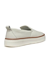 Zapatos slip-on de cuero blanco con punta redonda, parte superior texturizada y suela marrón. Cuentan con una lengüeta en el talón y detalles de costura sutiles.