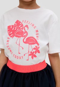 Witte katoenen t-shirt met een roze afbeelding van twee flamingo's en tropische bladeren, gecombineerd met een marineblauwe tule rok en een felroze tailleband.