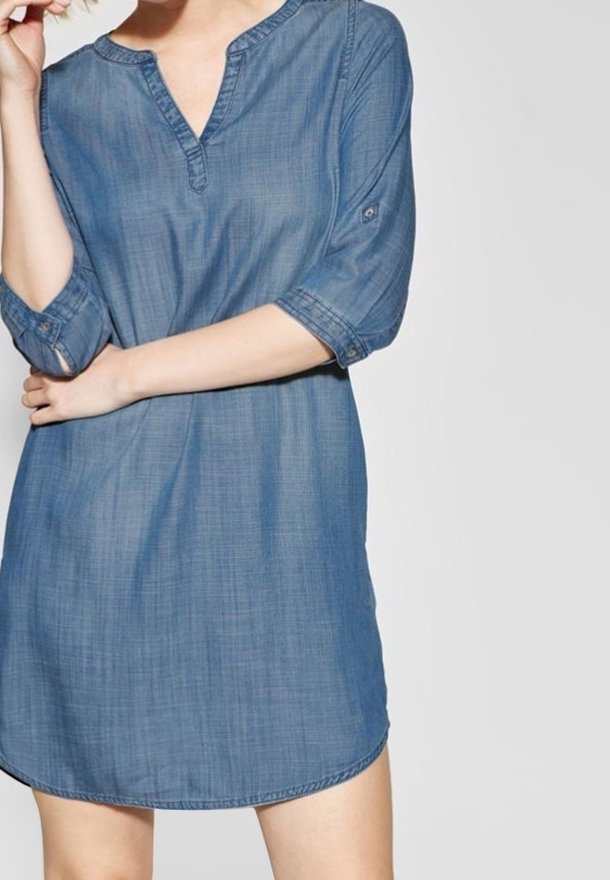 Denim-mekko, jossa on V-pääntie, 3/4-pituiset hihat ja kaareva helma. Vaalea sininen väri, jossa on hienovarainen rakenne. Hihoissa on napitusyksityiskohta.