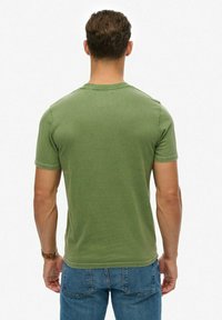 Camiseta de manga corta y cuello redondo en color verde oliva, hecha de algodón suave, presenta un corte relajado y detalles cosidos a lo largo de los hombros.