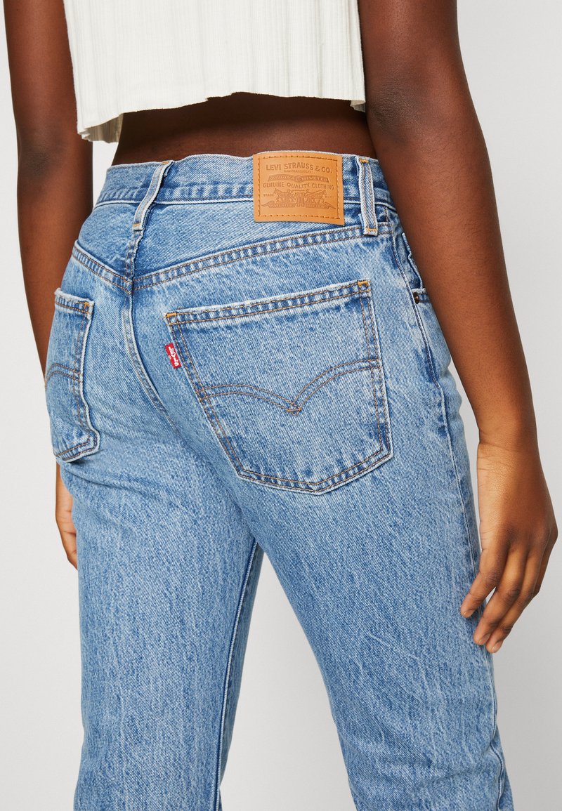 Helle blaue Denim-Jeans mit hoher Taille, die orangefarbene Nähte, ein Lederpatch auf der Rückseite und ein klassisches Fünf-Taschen-Design aufweisen.