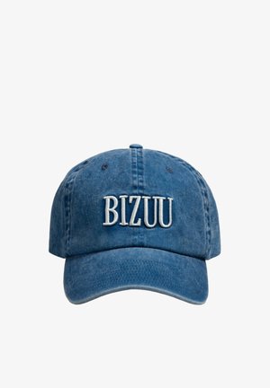 Vrouw draagt een blauwe pet met de tekst „BIZUU“, kantelt de pet naar voren met haar rechterhand, gekleed in een zwart topje.