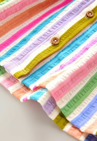Kangas berwarna-warni dengan pola garis-garis yang menampilkan nuansa pastel merah muda, biru, hijau, oranye, dan kuning, dengan tekstur ribbing dan kancing kayu.