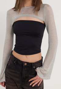 Top corto nero con maniche lunghe trasparenti argento, caratterizzato da un design con scollatura sul petto, abbinato a pantaloni a vita alta in denim scuro.