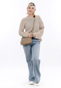 Beige knit sweater, light blue flared jeans, white sneakers, holding a small beige crossbody bag with textured surface and branding detail.