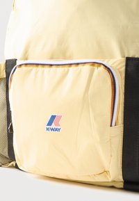 Τσέπη από κίτρινο ύφασμα σε σακίδιο πλάτης με πολύχρωμη επένδυση και λογότυπο K-Way σε μπλε και κόκκινο, μαύρα λουριά και δίχτυ στην αριστερή πλευρά.