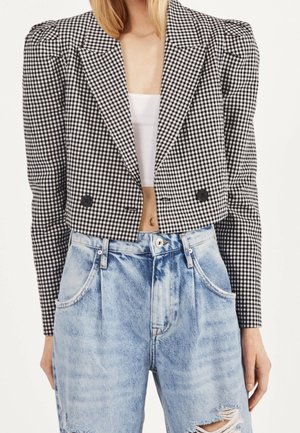 Femme portant un blazer court à carreaux noir et blanc, un crop top blanc et un jean déchiré bleu clair taille haute.