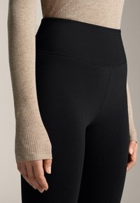 Leggings noirs taille haute en tissu extensible, avec une texture lisse et un design sans coutures, associés à un haut à manches longues beige côtelé.