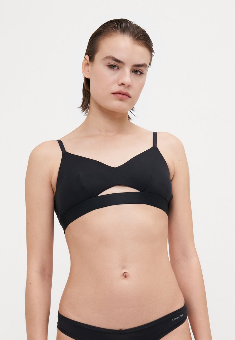 Soutien-gorge sans fil noir avec un détail découpé au centre, tissu lisse, bretelles fines et réglables, et une bande solide sous la poitrine.