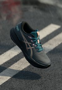 Sport shoe in dark gray with turquoise accents and pink laces. Features a textured upper, rounded toe, and supportive sole with grooves.