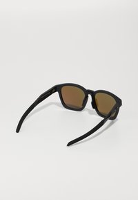 Sorte solbriller med mat finish, firkantet ramme og brune tonede linser. Udsmykket med slanke, elegante arme.