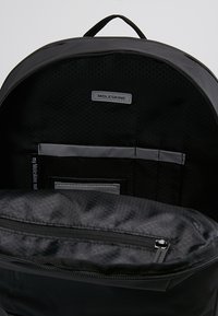 Zaino Moleskine nero con fodera a motivo esagonale, scomparto con zip e tasca organizzativa frontale con texture liscia.