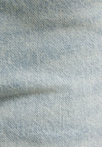 Light blue denim fabric with a twill weave, featuring a fine, textured surface and subtle variations in color and pattern.