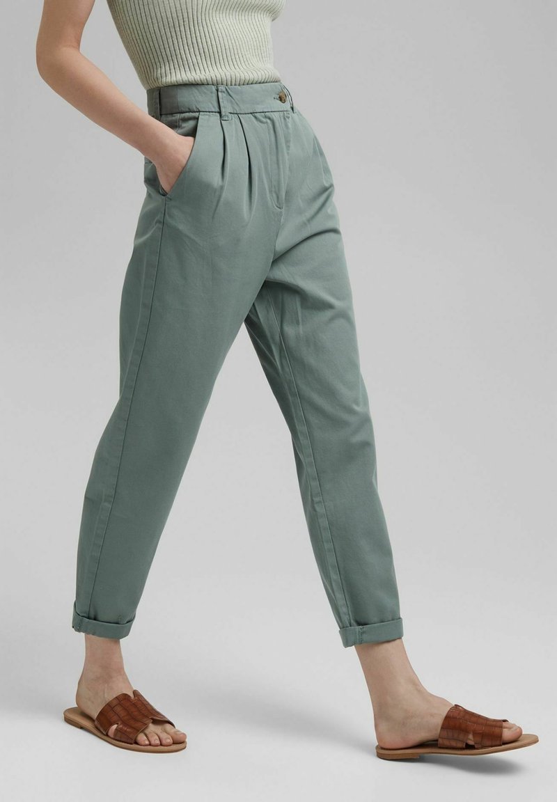 Light green belted trousers with pleats and rolled cuffs, shown alongside brown slip-on sandals with a woven texture.