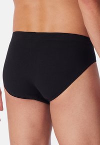 Schwarze Baumwollslips mit einer glatten Textur, elastischem Bund und klassischem Schnitt, die mit minimaler Naht für ein sauberes Design ausgestattet sind.