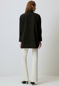 Black pinstripe shirt with a high collar and relaxed fit, paired with white flared trousers and gray high-heeled shoes.